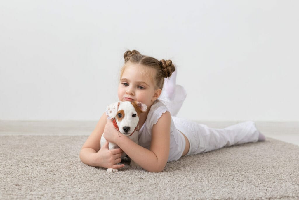 Little girl with her puppie lying on a white carpet
