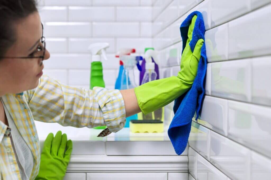 Woman cleaning and bleaching grout on bathroom tiles.