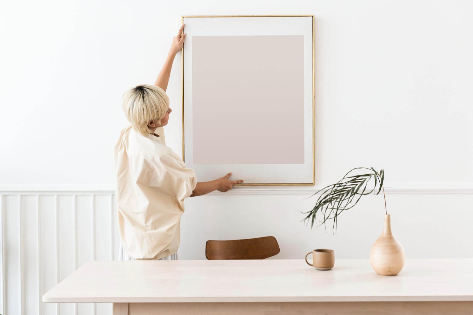 Woman hanging a photo frame on her recently cleaned wall after stains on walls removal