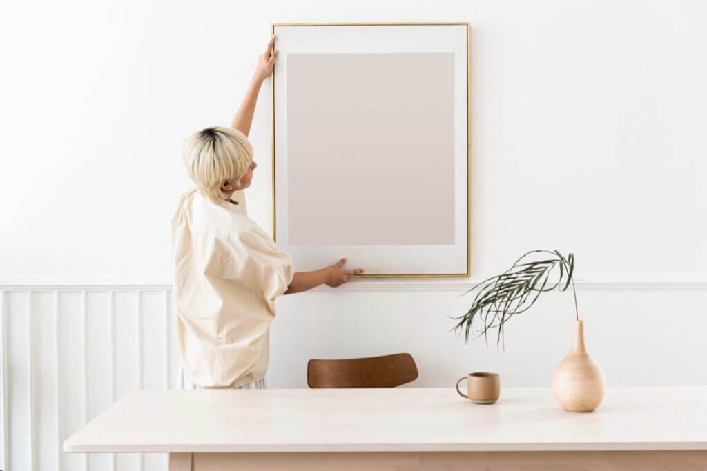 Girl hanging a photo frame on a white and pristine white wall at her home