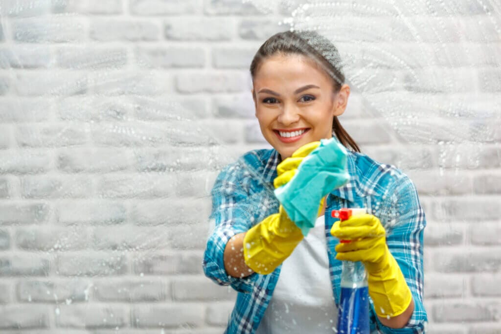 A young woman from the cleaning service smiling at the camera while cleaning the windows