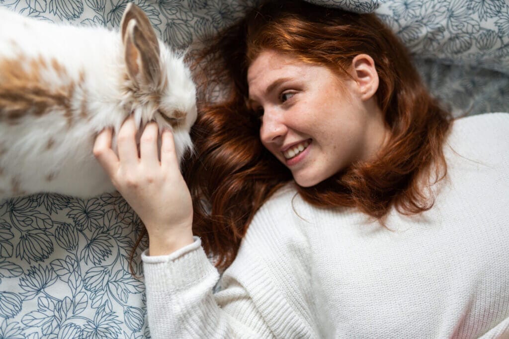 Smiling woman lying down while looking and caressing her pet bunny