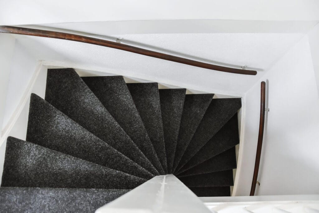 Beautiful grey spiral staircais with a black carpet on it