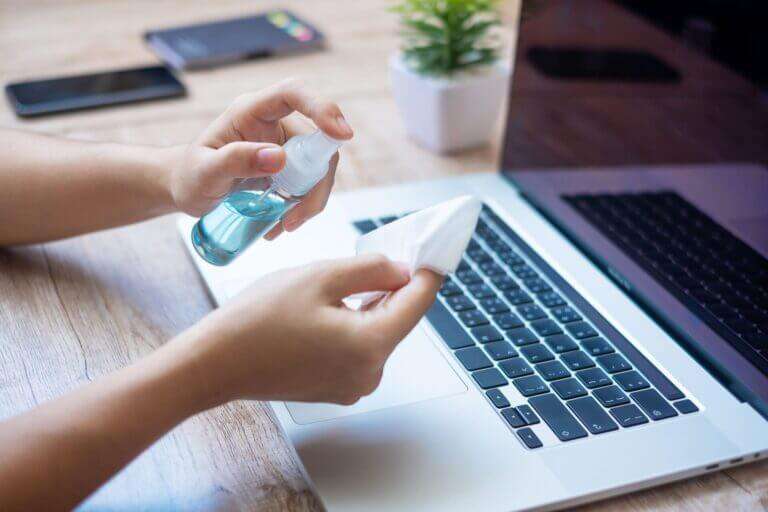 A person sanitizing a laptop with a damp cotton cloth after learning how to clean electronics